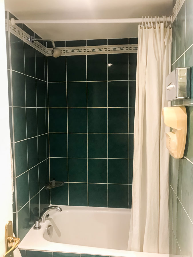 Salle de bain de la chambre témoin avant les travaux, une baignoire avec du carrelage vert foncé