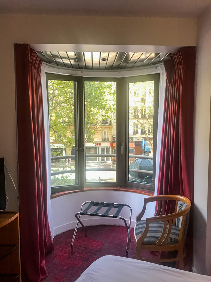 Fenêtre de la chambre témoin avec une chaise en bois, du lambris au plafond, des rideaux et une moquette rouge