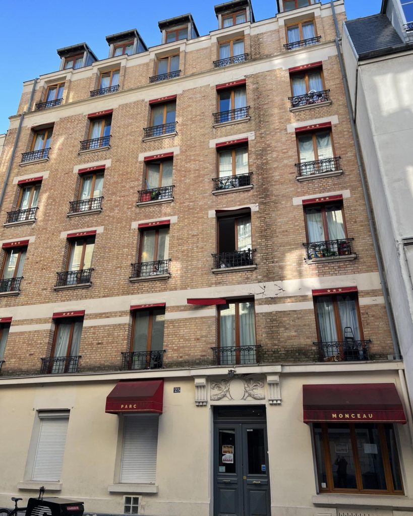 Vue de la façade de l'hôtel Pavillon Courcelles Monceau à Paris avec des brique et des devanture de fenêtre couleur bordeaux-rouge foncé.