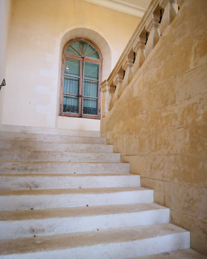Escalier de la maison familiale, en pierre de travertin avec une fenêtre aux bords arrondies.