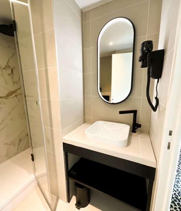 Vue de la salle de bain de la chambre de l'hôtel Villa Luxembourg avec son miroir, ses parois en marbre et son lavabo à la forme carré ainsi que sa robinetterie noir mat.