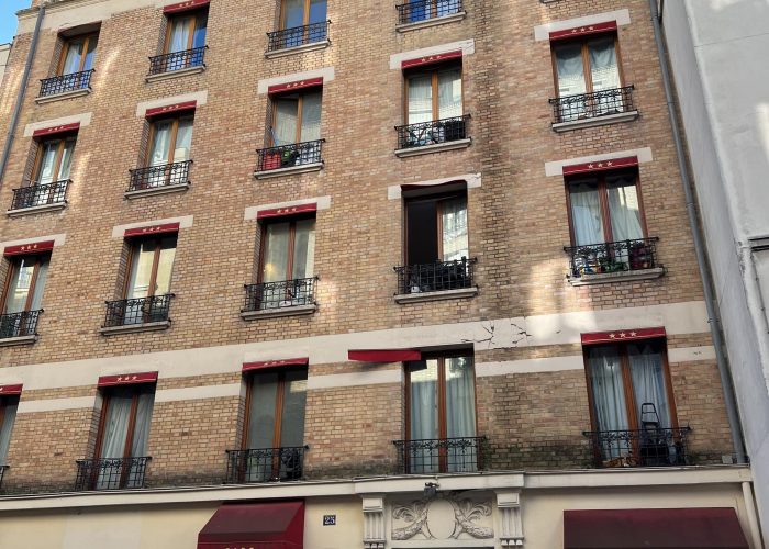 Vue de la façade de l'hôtel Pavillon Courcelles Monceau à Paris avec des brique et des devanture de fenêtre couleur bordeaux-rouge foncé.
